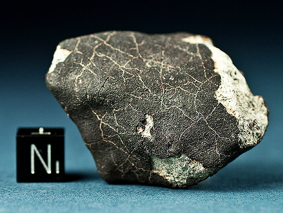 Vékony fekete olvadási kéreg és kontrakciós repedések kondrit meteoriton (Bensour meteorit). Az élek lekerekítettek, belső törésnyomok világosak.